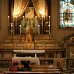 Two people sitting at a pew and praying in a church in Rome.